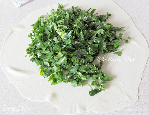 Раскатать тонкую лепешку. Она должна быть очень тонкой, прозрачной. Тесто очень мягкое и раскатывается легко. Можно  слегка препылить поверхность мукой, чтобы скалка не прилипала к тесту.  Начинку для каждой лепешки нужно готовить отдельно, так как, ранее посоленная трава может дать сок, а нам это не нужно. В отдельную мисочку отложить  порцию перченой травки со специями, добавить  брынзу и, если нужно - соль. Несколько капель растительного масла - не забыть. Эту начинку выложить на подготовленную лепешку толстым слоем. Распределить по всей поверхности.