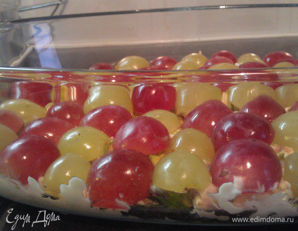 Следующим слоем выложить по всей поверхности половинки винограда, чередуя между собой красный и белый виноград.