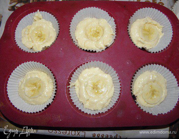 Теперь выкладываем в формочки. Для начала вставляем бумажные формочки, затем выкладываем тесто -  полторы чайной ложки теста, а сверху - кружок банана...