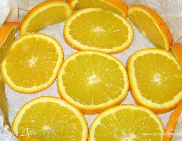 Бумагу для выпечки намочить и хорошо отжать. Выстелить  форму бумагой для выпечки, дно  и бока формы  выложить  кружочками апельсинов.