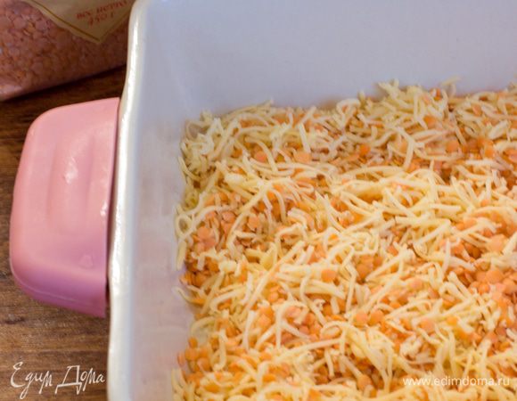 Форму для запекания смазать сл.маслом и первым слоем выложить сырую красную чечевицу, смешанную с половиной от всего количества натертого сыра.