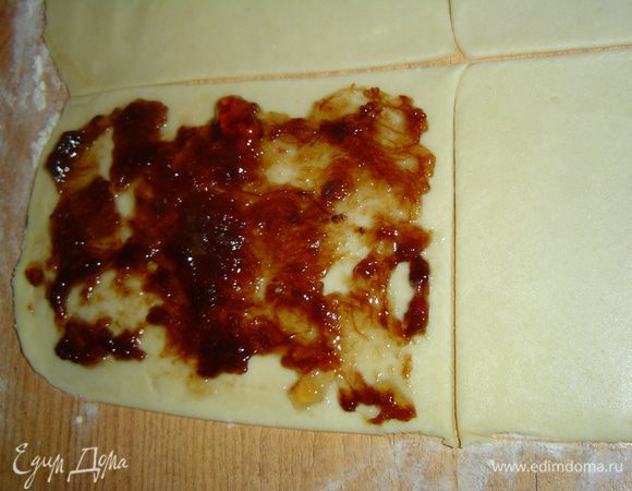 Через час тесто достаем из холодильника, делим на три части и тонко раскатываем. Режем тесто на квадратики, сверху выкладываем повидло(или густое варенье),