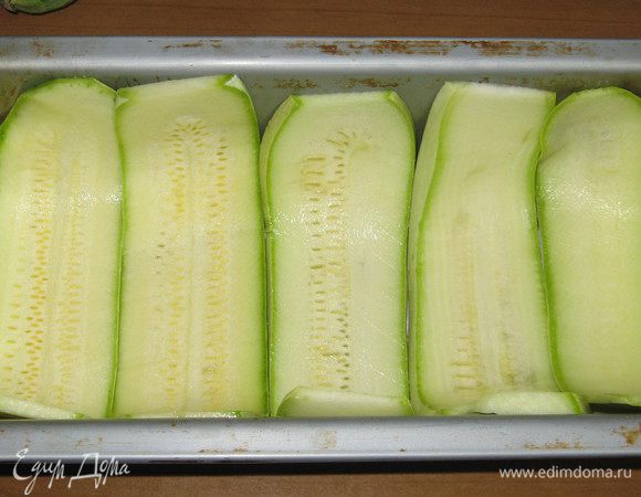 Форму для запекания смазать оливковым маслом и выложить дно пластинками цукини.