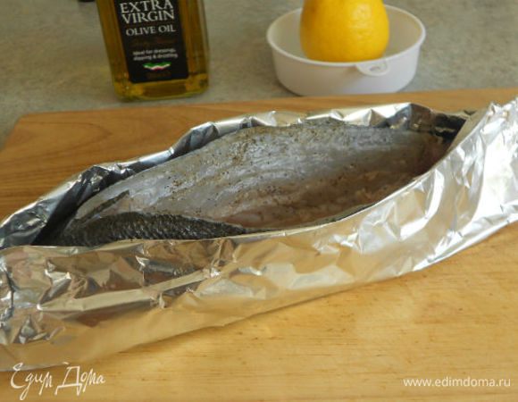 При помощи 2 слоёв фольги зафиксируйте рыбу в вертикальном положении, оставив верхний разрез открытым. Не забудьте предварительно хорошо смазать оливковым маслом внутреннюю сторону фольги и особенно рыбий хвост. Иначе он высохнет.