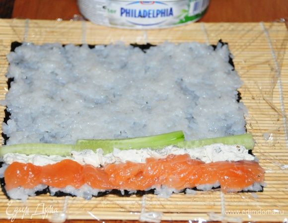 Первый ролл – Футомаки с форелью:
На нори руками выкладываем тонкий слой риса, тщательно разравниваем. Руки постоянно смачиваем в уксусе, т.к. рис очень липкий! С краю, который ближе к Вам выкладываем начинку: кусочки рыбы, рядом с ней полосочку сыра «Филадельфия», огурчик. Можно добавить маленькие капельки васаби.
