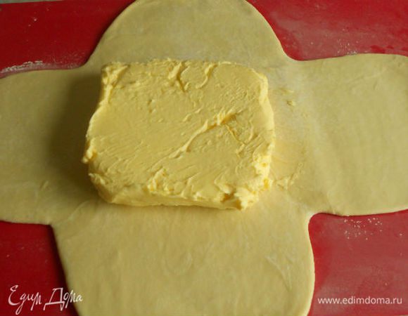Надрежьте тесто крестообразно, подсыпьте муки и раскатайте тесто скалкой так, чтобы середина пласта была толще, чем края. Это важно! В центр пласта положите заготовленную лепешку из масла и муки.
