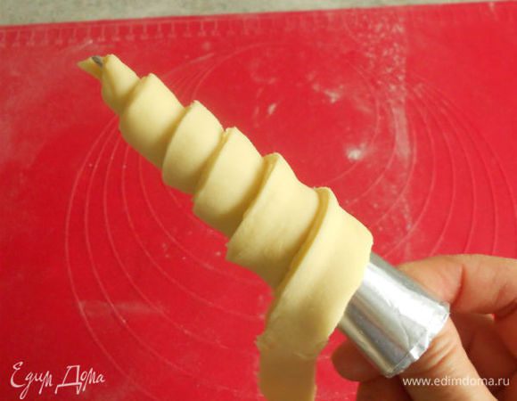Дальше раскатывать и складывать тесто не рекомендуется, так как тонкие слои могут разорваться, вследствие чего масло перемешается с тестом и изделия получатся с маленьким количеством слоев. Готовое тесто раскатайте в прямоугольный пласт толщиной около 5–6 мм, нарежьте его на длинные полосы шириной 1,5–2 см. Возьмите в правую руку конусную жестяную или бумажную трубочку, а в левую — конец полосы теста, прикрепите его к узкому концу трубочки. Поворачивая правой рукой трубочку, расположите полоску по спирали, следя за тем, чтобы один край теста находил на другой. Заворачивать полоску теста надо по направлению от узкой части конуса к широкой, при этом лента растянется до толщины 3–4 мм. Всего надо сделать 5–6 витков.