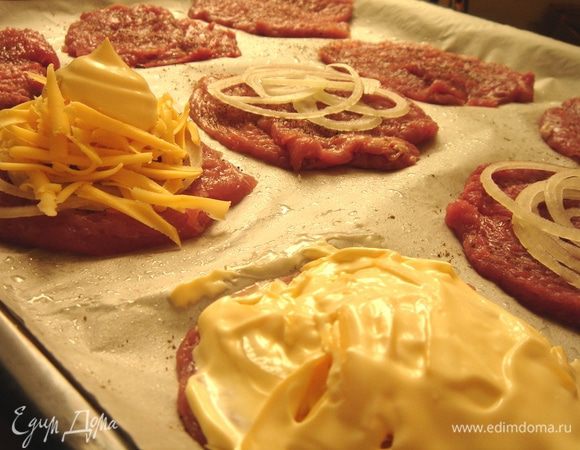 Выложить на противень кусочки мяса. Посолить и поперчить их с одной стороны. Лук тонко нарезать кольцами или полукольцами, сыр натереть на крупной тёрке. На мясо выложить лук, затем сыр и покрыть эту пирамиду майонезом.