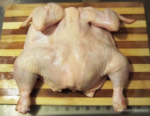 Уложить на разделочную доску. Разрезать цыпленка вдоль грудки и раскрыть, как книжку.