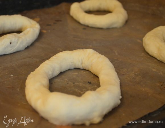 В каждом шарике делаем дырочку, растягиваем в кольцо примерно 10-12 см в диаметре. Выкладываем на противень, застеленный бумагой, смазанной маслом. Баранки должны быть на расстоянии друг от друга, накрыть полотенцем и дать постоять еще 40 минут.