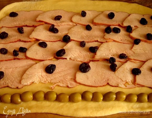 Раскатать тесто в прямоугольник. У края выложить в ряд оливки. На остальное тесто,отступив от другого края 10 см, разложить ветчину, поверх ветчины одной полосой выложить пластинки бекона и разбросать отжатый изюм. При желании можно повторить ряд оливок. Свернуть тесто в плотный рулет, начиная с оливок,оставив незавернутыми 10 см теста.