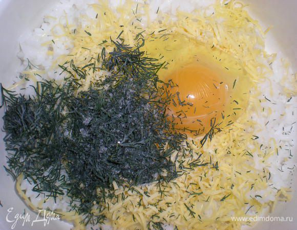 В слегка остывший рис добавить одно яйцо, половину натертого твердого сыра, укроп.