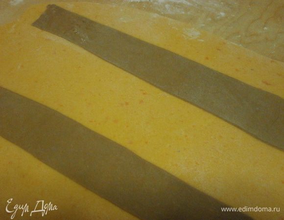 Рабочую поверхность присыпать мукой и раскатать оранжевое тесто толщиной не более 2 мм. Также раскатать и тёмное тесто. Нарезать из тёмного теста полоски шириной 2 см. Смочить одну сторону водой и наложить на светлое тесто на расстоянии друг от друга 5 см. Прокатать аккуратно, стараясь не нарушать ровность полосок....