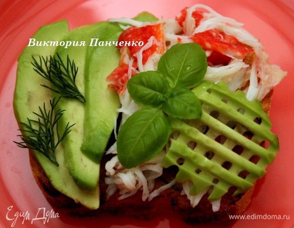 Выложить на хлеб ломтики авокадо и разобранное на волокна крабовое мясо. Украсить базиликом.