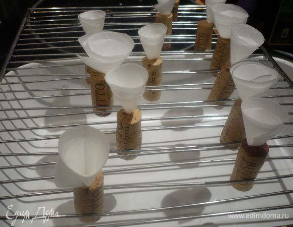 Делаем формочки для елочек. 12 винных пробок надрезаем вдоль острым ножом. Для кулечков складываем пекарскую бумагу в шесть раз, обводим какую-нибудь круглую емкость диаметром примерно 6 см. Еще раз делаем тоже самое. Вырезаем круги. Накладываем один круг на другой и разрезаем до середины, сворачиваем кулек. У нас получается в результате 12 кульков. Кончик каждого кулечка вставляем в разрез на пробке, пробку закрепляем между прутьями небольшой решетки для пирогов и ставим на форму для запеканки, чтобы в случае падения «поймать» наш кулек и содержимое (мне повезло и, когда кулечки в духовке попадали, бисквит уже успел схватиться.) Таким же образом вырезаем кулечки диаметром 12 см и вкладываем их в отверстия упаковки из-под яиц (можно делать кульки в один слой, форма держится хорошо).