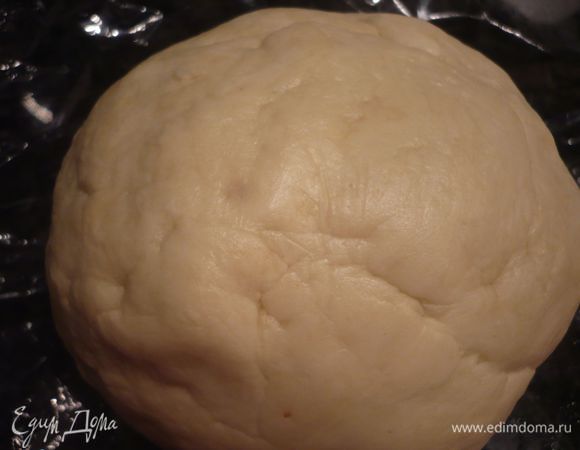 При помощи насадки для вымешивания теста смешиваем 200 г муки со сливочным сыром и порезанным на куски маслом, вводим 30 мл холодной воды, а затем добавляем еще 50 г муки. Кладем в пишевую пленку и приминаем тесто, делаем его площе. Ставим в холодильник на 1 час.