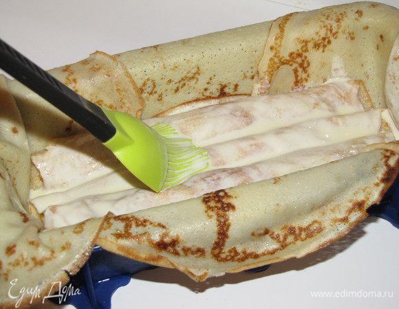 Форму для выпечки выложить блинами с четырех сторон так, чтобы края блинов свисали за пределы формы. Далее выложить рулетики из блинов. Желательно, чтобы длина рулетиков совпадала с длиной вашей формы. У меня получилось два слоя по три рулетика. Каждый слой хорошо промазать заливкой.