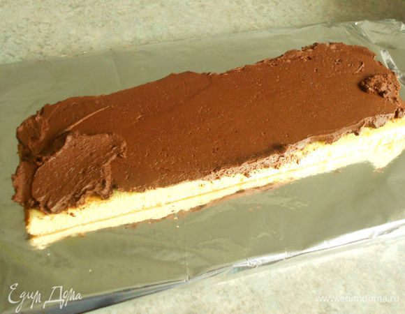 Разделочную доску накрыть фольгой или пергаментом, положить на неё полоску светлого коржа. 4 ст. л. ганаша выложить на бисквит и равномерно распределить. 