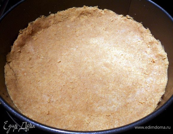 Разъемную форму слегка смазать сливочным маслом, выложить песочную крошку и хорошо утрамбовать, формируя бортики (не обязательно очень высокие, можно 2 - 3 см., а можно вообще без них). Форму (дно и небольшая часть бортиков, на стыке разъема) лучше завернуть фольгой. Основу поместить в заранее разогретую до 175 -180 С духовку и выпекать около 10 минут.  Остудить. Огонь уменьшить до 120 -130.