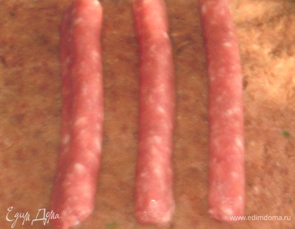 Выложить фарш  на бумагу для выпечки в виде прямоугольника, в центр положить колбаски и свернуть рулетом. 