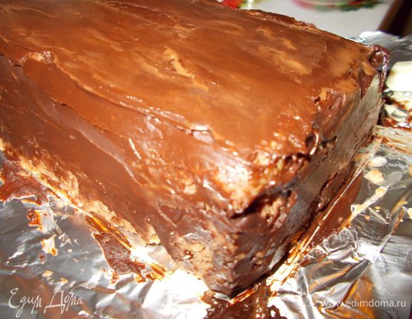 Достаем наш торт из холодильника.Выкладываем его на доску,предварительно сняв целлофановую пленку.Освобождаем торт от фольги и покрываем его глазурью.Глазурь застывает очень быстро,поэтому наносить её нужно оперативно :)).Чтобы выровнять поверхность глазури,окунаем узкую металлическую лопатку в горячую воду и плоской поверхностью разглаживаем её.Если глазурь легла полосками,это очень хорошо потому,как торт будет больше похож на полено.:)).