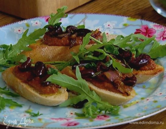 Тосты слегка натереть чесноком, сбрызнуть оставшимся оливковым маслом, разложить на них пюре из перца и фасоли, оставшийся обжаренный лук и оливки, украсить листьями базилика и руколой.