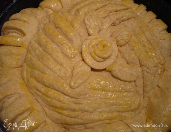 То же самое проделываем с остальными пятью частями теста. В результате наш хлеб выглядит так. Если Вы захотите сделать розу для украшения центра, разделите отложенное ранее тесто на 9 кусочков, каждый из которых раскатайте, из пяти кусочков сделайте цветок розы, для этого сверните первый трубочкой и оберните эту трубочку – центр розы - по очереди остальными «лепестками». Из остальных 4 кусочков сделайте листья, для этого нанесите при помощи ножа характерный орнамент. Смазываем хлеб яйцом. 