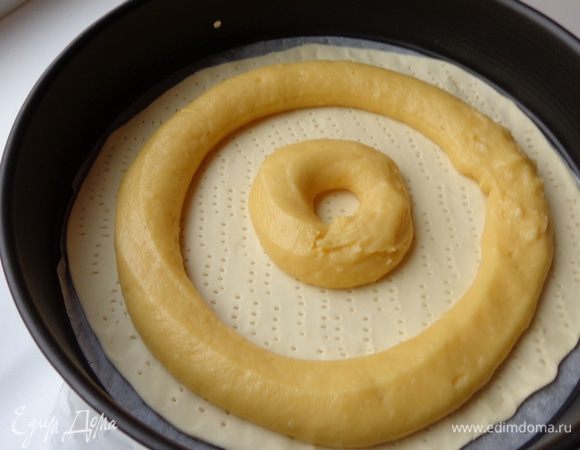 Сделать заварное тесто: вскипятить 1 стакан воды с солью и 100г сливочного масла, добавить муку. Прогреть массу на слабом огне при постоянном помешивании. Когда масса скатается в единый ком и будет легко отделяться от краев кастрюли, снять кастрюлю с огня. Немного остудить и добавить по одному 4 яйца, каждый раз тщательно вымешивая тесто, но не взбивая его.
Часть готового теста положить в кондитерский мешок с насадкой 2,5 см в диаметре и выложить его по внешнему краю слоеного теста, отступив на 1 см.

Дальше один из шеф-поваров предлагал сделать еще 2 круга среднего и маленького размеров. НО: он предупреждал,  что чем больше заварного теста выложено на основу, тем труднее поймать то время, когда все заварное тесто достаточно пропеклось, но не пересушилось. Поэтому советовал на первых порах  ограничиться только большим внешним кругом.

Я решила рискнуть, но т.к. я недостаточно продвинутый мастер, сделала только два круга.
