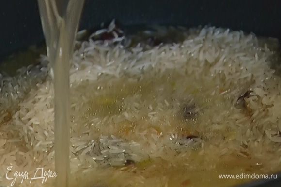 Всыпать рис, влить 400 мл горячего бульона, так чтобы рис был покрыт, и накрыть сотейник крышкой.