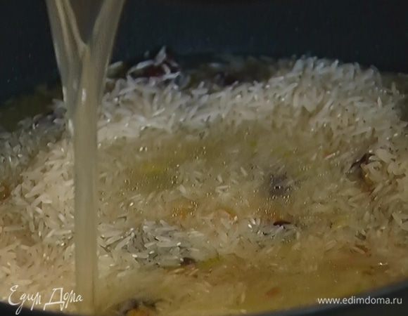 Всыпать рис, влить 400 мл горячего бульона, так чтобы рис был покрыт, и накрыть сотейник крышкой.