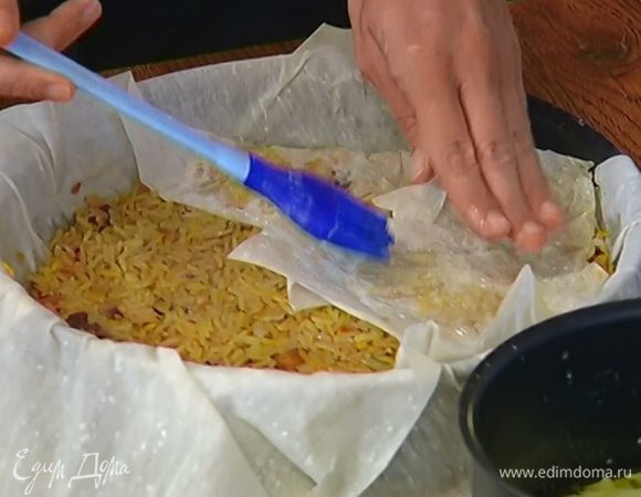 Сковороду смазать растопленным сливочным маслом, выложить пласт теста фило так, чтобы свешивались края, смазать его маслом, затем выложить еще один слой фило, смазать маслом, выложить сверху плов и накрыть свисающими краями теста.