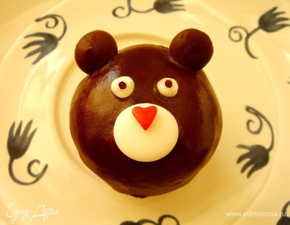 Бананово-кофейные кексы окунуть в шоколадную глазурь,приготовленную из растопленного шоколада с добавлением сливочного масла. Из пакетов с белым и чёрным шоколадом выдавить на пергамент плоские "таблетки"(можно использовать готовый шоколад или глазурь в таблетках). Убрать в холодильник на 10 минут, а потом былые таблетки уложить на нижнюю часть кекса, а для чёрных сделать тонким ножом небольшие надрезы в верхней части кекса и вставить таблетки-ушки. На белую таблетку-мордочку капнуть белого шоколада и прикрепить на него сахарное украшение ( сердечко,звёздочку и т.д.). Ещё две белые капли будут глазами,а совсем маленькие чёрные- зрачками. Мишка готов!