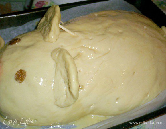 Оставшееся тесто раскатываем овалом большего размера, наматываем на скалку и переносим на "поросенка", скрепляем верхний и нижний края теста, подворачиваем шов под низ. Руками придаем кулебяке очертание поросенка. Не забываем про ушки и хвостик. Ушки желательно не делать слишком тонкими, чтоб они не прогнулись под своим весом. Пятачок вырезаем из кусочка красного перца, глазки - крупные изюминки. Ушки и пятачок прикрепляем с помощью зубочисток или спичек, предварительно убрав с них серу. Смазываем поросенка взбитым яйцом и делаем маленькие дырочки, чтоб выходил пар. 