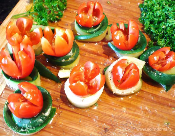 Духовку разогреть до 180 градусов. Помидоры надрезать сначала крест-накрест, потом надрезать еще раз, чтобы получилось восемь лепестков. Цукини разрезать вдоль и свернуть в рулетик, на каждый рулетик посадить по помидору.  Посолить, поперчить, сбрызнуть лимоном и оливковым маслом. 