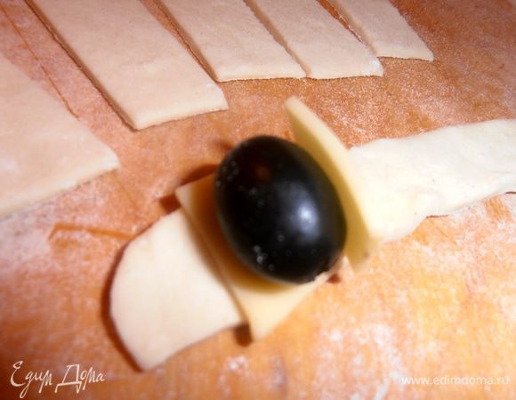 Каждую полоску делим пополам.На край теста кладём кусочек сыра,затем оливку боком и сверху снова сыр.
