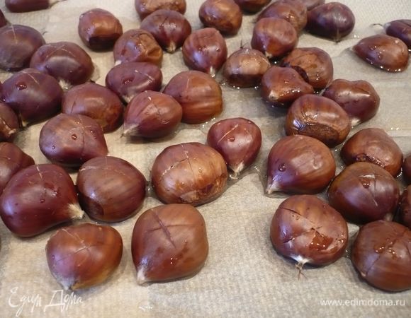 Духовку разогреваем до 120 градусов. Каштаны промываем холодной водой и надрезаем выгнутую часть крест-накрест. Укладываем на противень, сбрызгиваем примерно 100 мл холодной воды. Ставим в духовку на 40 минут. 