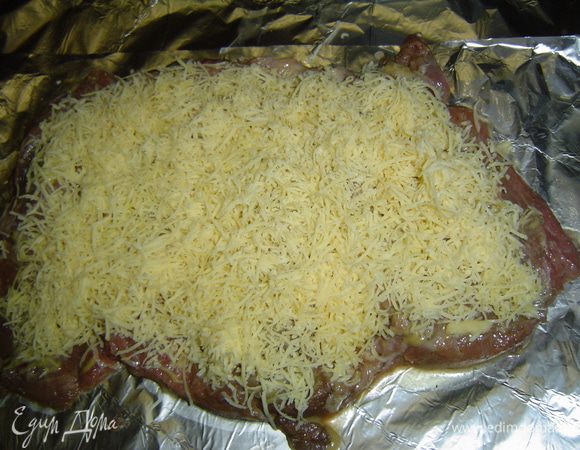 Достаем мясо из маринада, выкладываем его на фольгу, смазываем горчицей и посыпаем натертым сыром.
