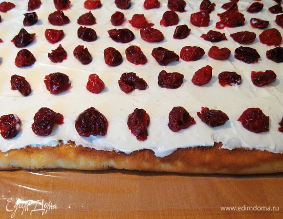 Бисквит разворачиваем и пропитываем сиропом. Распределяем по нему крем. Сверху выкладываем вишню.