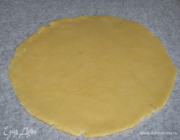 Достать тесто из холодильника, разделить на две неравные части.  Большую часть раскатать в круг и перенести на противень, застеленный пекарской бумагой.