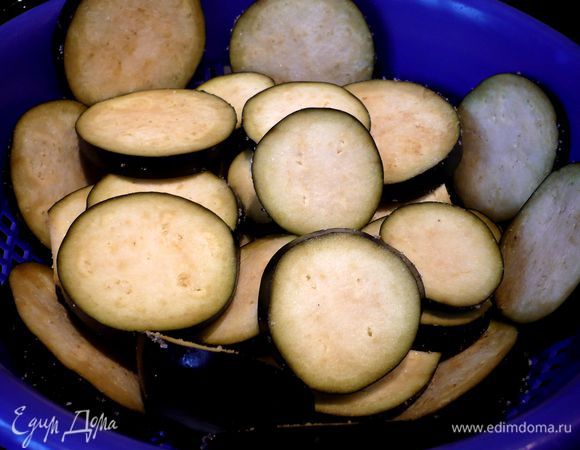 У баклажанов срезаем кончики, нарезаем их кольцами примерно 1 см шириной, хорошо обтираем солью и укладываем слоями на сито на полчаса.