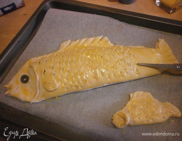 Лист застелить бумагой, смазать оливковым маслом. Перенести "Рыбу". Из оставшегося теста и начинки можно приготовить пирожки в виде рыбок. Смазать поверхность слегка взбитым вилкой желтком. С помощью ножниц нарезать "чешуйки". Отверстия необходимы, чтобы выходил пар во время выпечки и рыбка хорошо пропечется. Выпекаем при температуре 180 градусов 50-60 минут. 