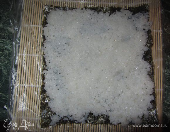 На циновку положите лист нори (если хочется, чтобы получились небольшие роллы, то половину листа нори), выложите тонким слоем рис (я делаю это ложкой, предварительно смачивая в холодной воде). Циновку обычно я оборачиваю в пищевую пленку, чтобы рисинки не застревали.