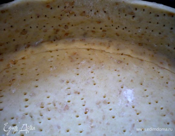 Разогреем духовку до 200 градусов. Смажем сливочным маслом форму диаметром 28 см. Раскатаем тесто и вырежем круг соответствующего диаметра. Из обрезанного теста сделаем высокие бортики (в зависимости от высоты формы). Проткнем вилкой бортики и низ тарта.