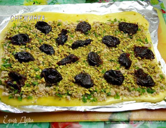 Снимаем пищевую плёнку. Распределяем курицу с зеленью, немного вдавливая в пласт. Верхний край оставляем немного свободным. Сверху – фисташки, затем – чернослив.