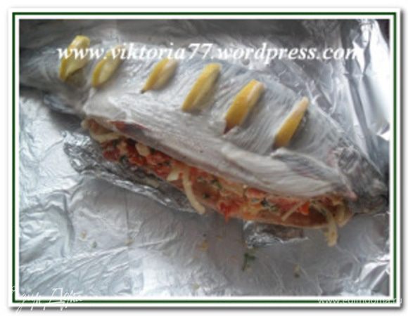 Противень выложить фольгой, смазанную маслом. Выложить на противень рыбу. Сделать валик из фольги и положить под брюшко форели, где будет начинка, чтобы приподнять немного рыбу и чтобы при запекании не вытек сыр. Наполнить брюшко форели начинкой из сыра и помидор. Можно скрепить зубочистками (я этого не делала). У рыбы сделать вдоль туловища надрезы и выложить в них по ½ дольки лимона. Рыбу смазать растительным маслом или майонезом.