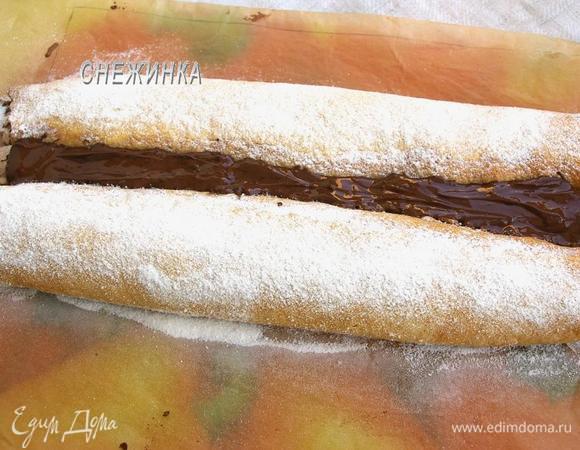 Снимаем заготовку с противня вместе с бумагой. Рулеты посыпаем сахарной пудрой, а расстояние между ними заполняем растопленным шоколадом.