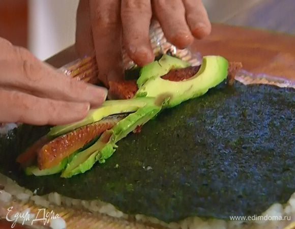 На край листа нори выложить немного огурца, авокадо и угря, свернуть плотный рулет, прижимая его руками после каждого оборота.