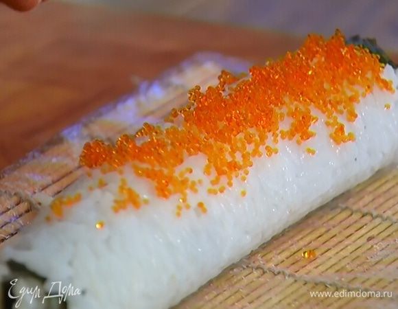 Переложить рисовый рулет с коврика на рабочую поверхность и намазать икрой, а затем порезать на порции.