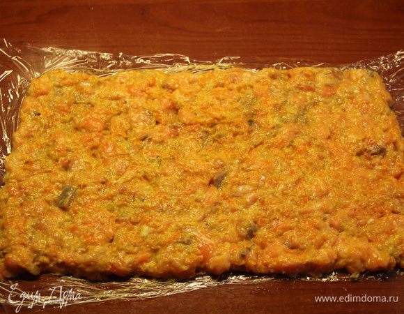 И вот теперь начинается самое интересное =) Выложить фарш прямоугольником на пищевую пленку. Позже нам нужно будет завернуть его в рулет. Когда я это начала делать, рулет-то заворачивался, но фарш потихоньку сдвигался с пищевой пленки, и когда я это заметила, 2 см.рулета было уже на столе. К тому же, потом нам еще переносить рулет на противень. Так что лучше сразу подстелить под пищевую пленку бумагу для выпечки так, чтобы рулет после скрутки оказался на ней, и было проще перенести его.=)