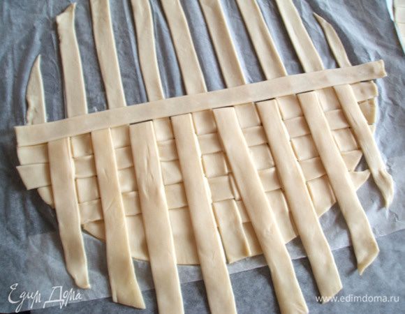   Перед  выполнением "плетёнки" тесто хорошенько охладить. На листе пергамента расположить рядом два пласта теста. Разрезать их на полосы шириной около 1,5 см. "Плетёнку" будем делать на первом пласте теста, "вплетая" в него полосы от второго пласта. 
   Откинуть назад четные полосы первого пласта теста, взять полоску от второго пласта и положить её перпендикулярно отогнутым полосам.